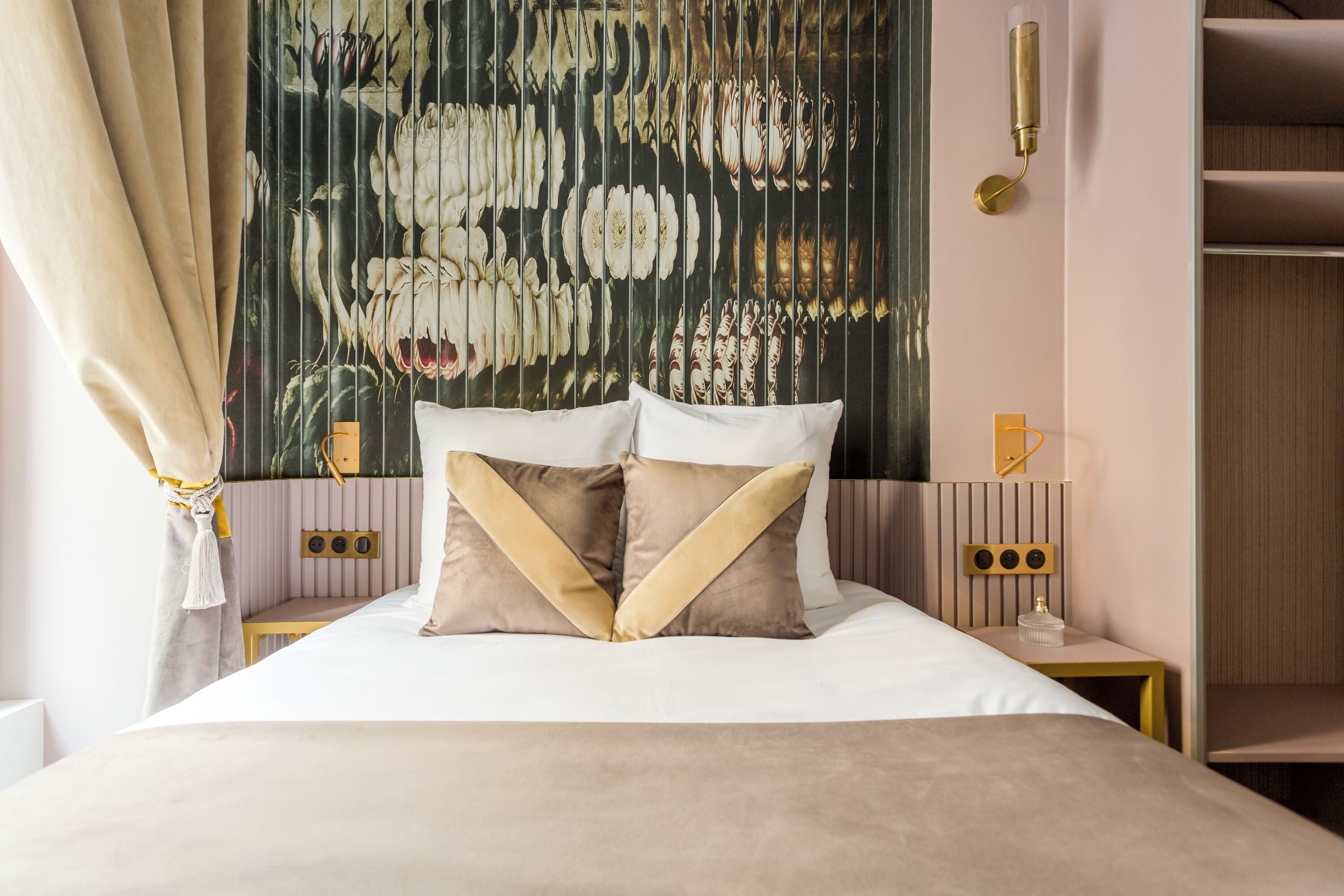 A neatly made bed with two decorative pillows, a wall tapestry, bedside lamps, and a small bedside table.