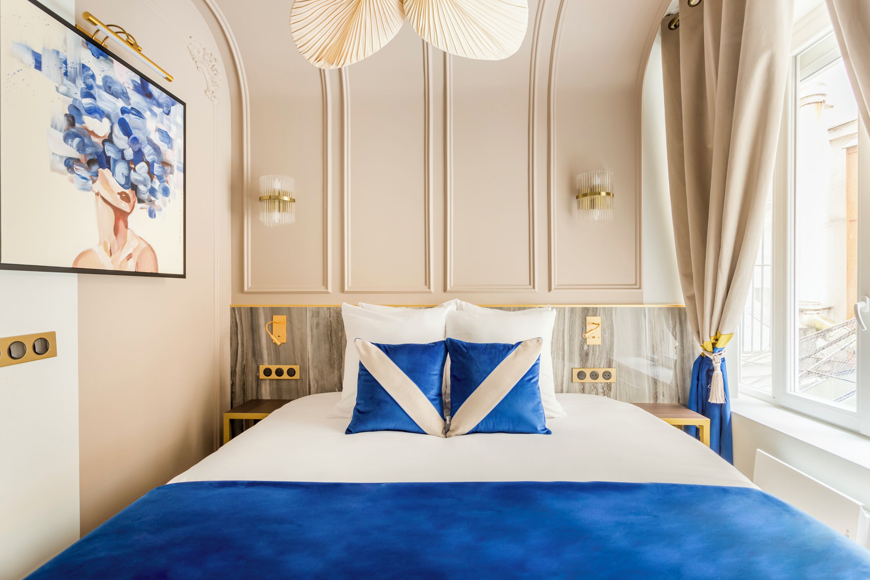 A bedroom with a bed, a painting, a chandelier, and a window with curtains.
