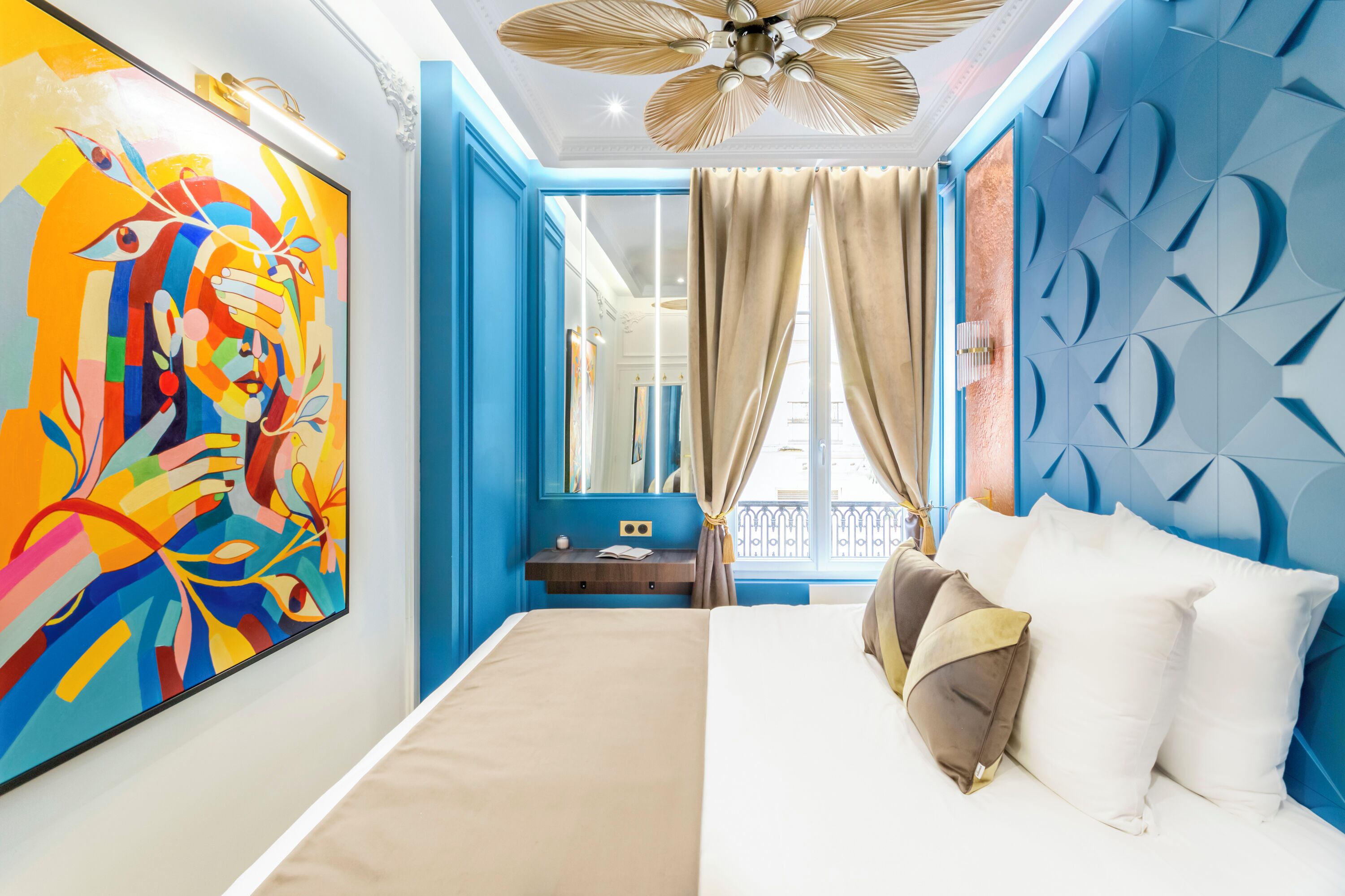 Habitación de hotel moderna con una cama grande, un ventilador de techo, un cuadro abstracto llamativo y vistas al balcón exterior.