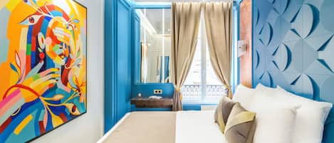 Habitación de hotel moderna con una cama grande, un ventilador de techo, un cuadro abstracto llamativo y vistas al balcón exterior.