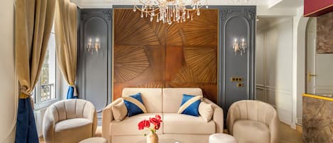 Una sala de estar lujosa con un sofá color beige, dos sillones, una mesa de centro de vidrio y un panel decorativo en la pared.