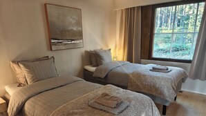 Een kamer met twee bedden, een schilderij aan de muur, een raam met gordijnen en een houten vloer.