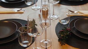 Een eettafel gedekt met zwarte borden, heldere wijnglazen en zwarte placemats.
