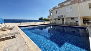 A swimming pool with lounge chairs and a building with air conditioning units. - 41 KAP - Stay Paradise Apartment (Paralimni)