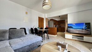A modern living room with a grey sofa, a wooden coffee table, a TV, and a kitchen in the background. - 41 KAP - Stay Paradise Apartment (Paralimni)