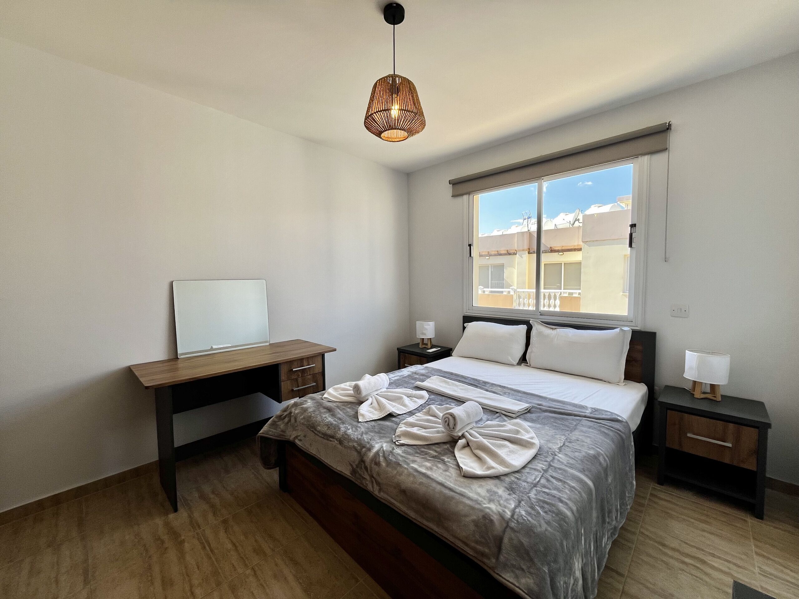 A bedroom with a bed, a desk, a window with a view, and a hanging light fixture.