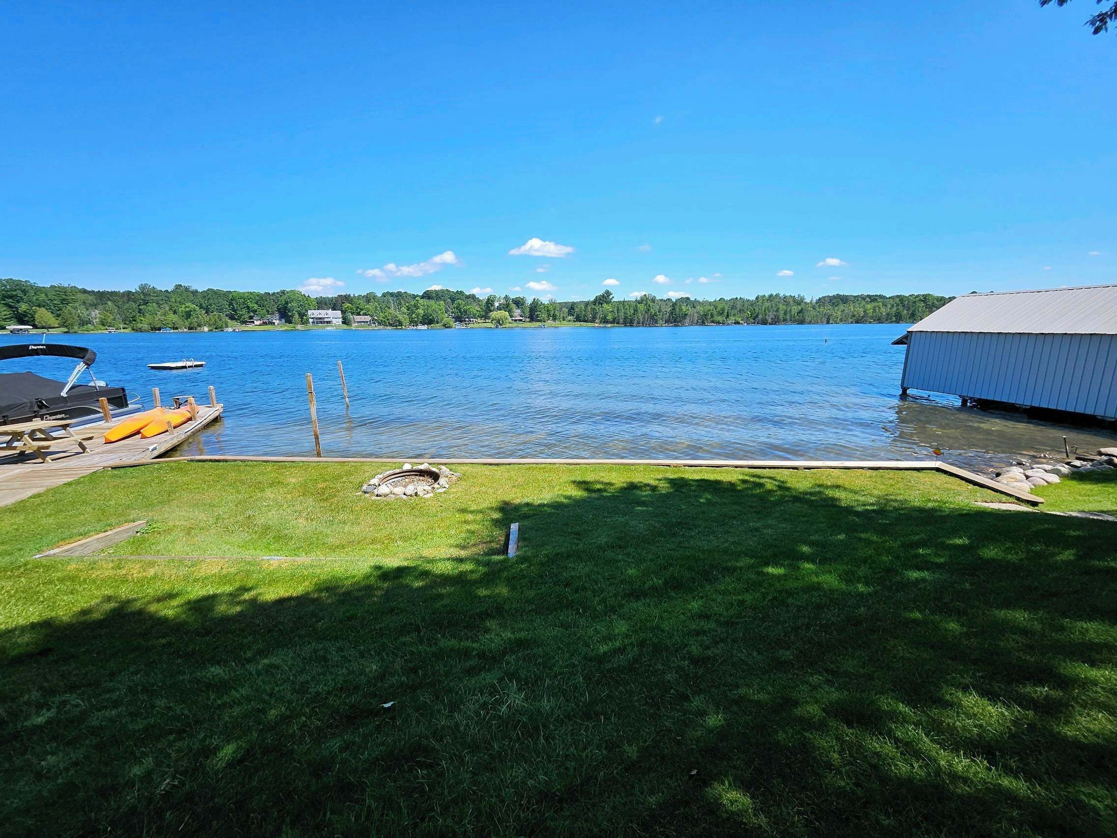 A lakeside dock with a boat, a grassy area, and a small shed.