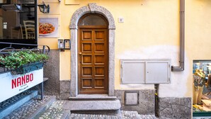 A building with a stone entrance, a wooden door, and a sign reading "NANDO." - Mansarda Mella by Wonderful Italy (Bellagio)