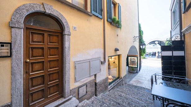A narrow street with a stone archway leading to a building with a wooden door and shutters. - Mansarda Mella by Wonderful Italy (Bellagio)