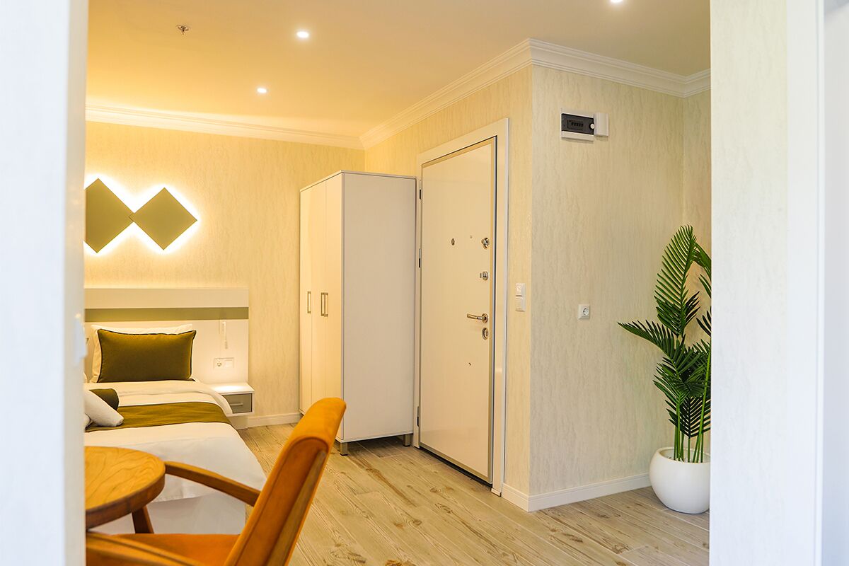 Une chambre d’hôtel comprenant un lit, une table de chevet, une chaise, une armoire et une plante en pot.