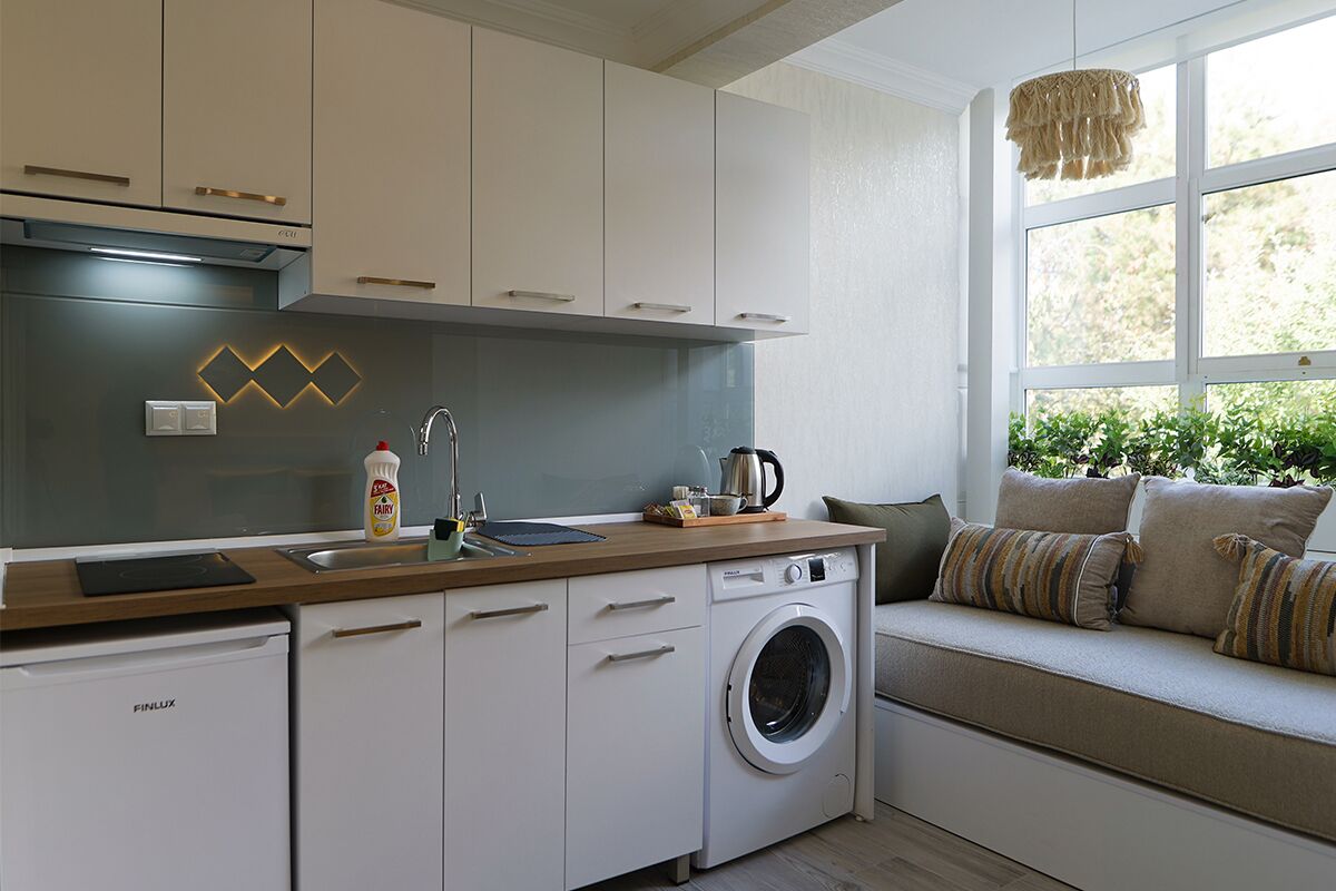 A compact kitchen with a washing machine, a sink, and a window seat with cushions.