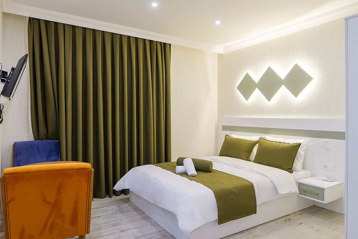 A hotel room with a bed, a nightstand, a chair, and a wall-mounted light fixture.