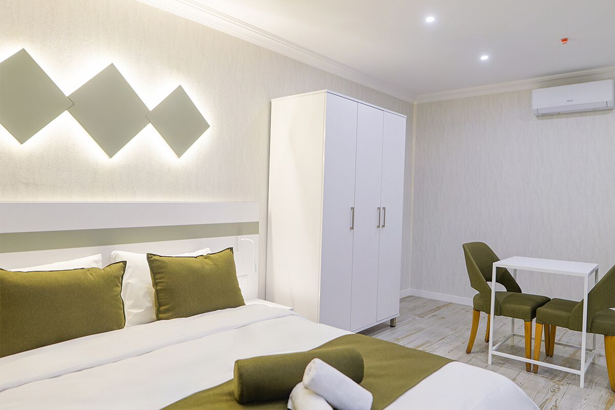 A hotel room with a bed, a wardrobe, a desk with two chairs, and an air conditioning unit.
