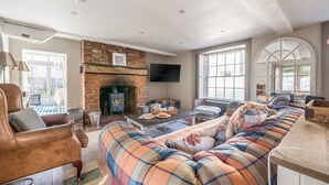 Un salon chaleureux avec une cheminée, des fauteuils confortables et de grandes fenêtres.