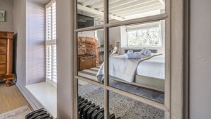 Une chambre avec une grande fenêtre, une cheminée en briques et un lit recouvert de draps blancs.
