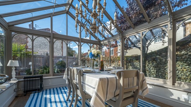 Une véranda avec une table dressée pour le repas, de grandes fenêtres et un lustre.