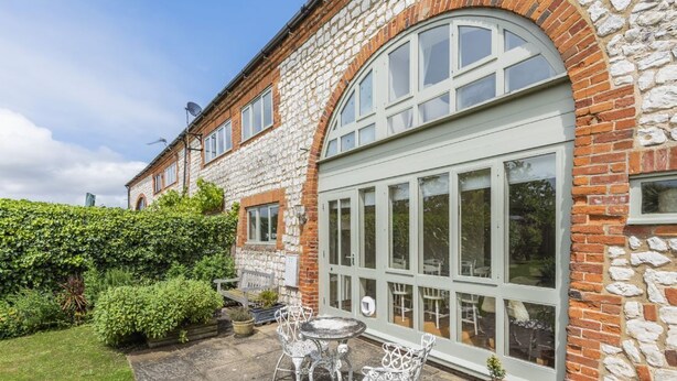 Ein Steinhaus mit einem großen Bogenfenster und einer Terrasse mit Tisch und Stühlen.