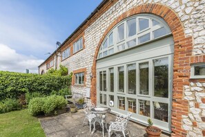 A stone building with a large arched window and a patio with a table and chairs. - Crowberry Barn - sleeps 6 guests  in 3 bedrooms (Burnham Market)