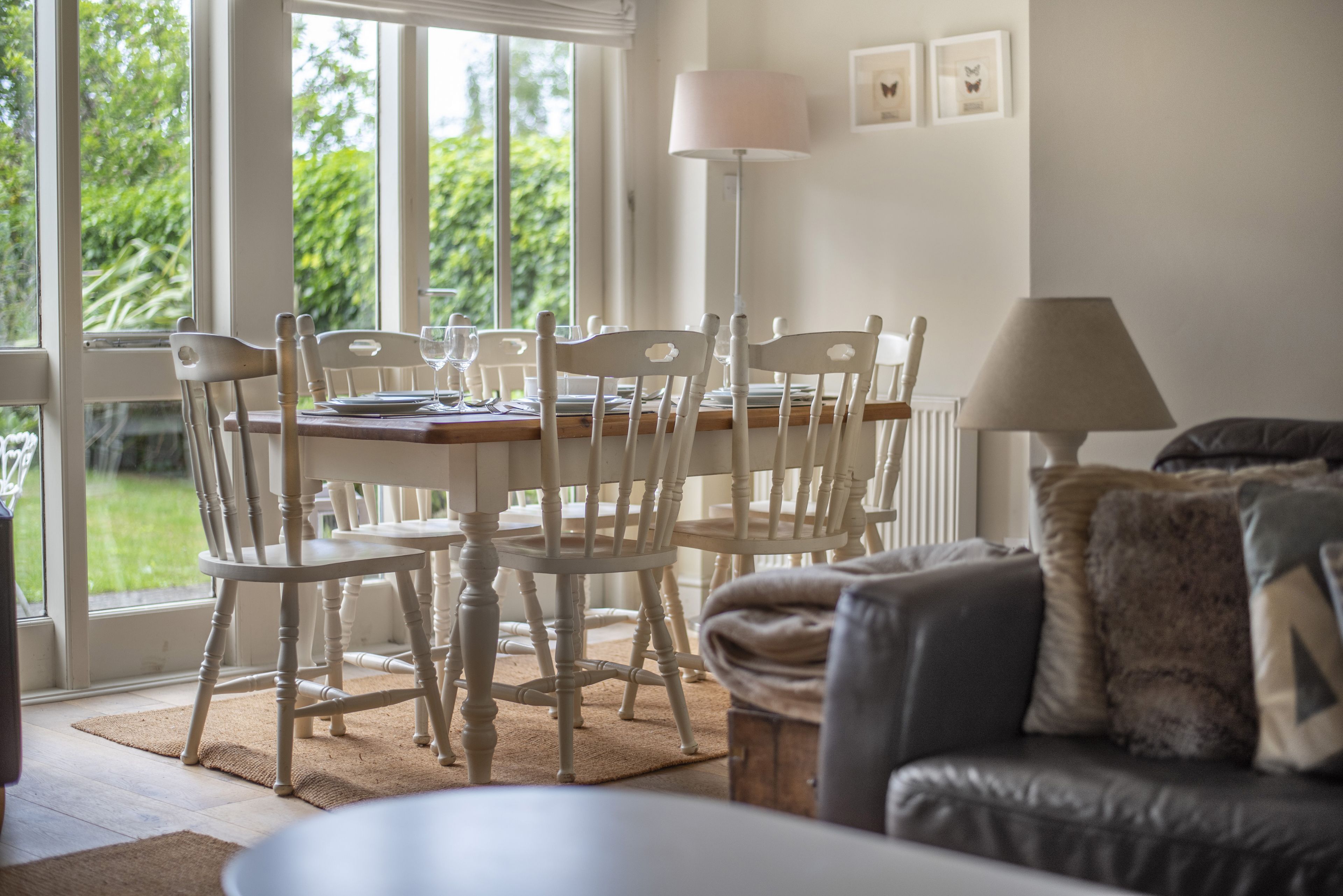 Un coin repas avec une table dressée pour quatre personnes, entourée de chaises blanches, d’une lampe et de tableaux encadrés accrochés au mur.