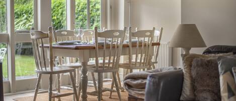 Un coin repas avec une table dressée pour quatre personnes, entourée de chaises blanches, d’une lampe et de tableaux encadrés accrochés au mur.