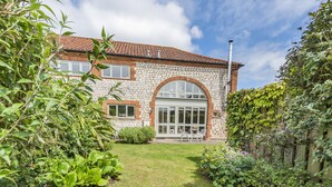 Ein Haus aus Stein mit Ziegeldach, einem großen Bogenfenster und einem Garten mit verschiedenen Pflanzen und einer Rasenfläche.
