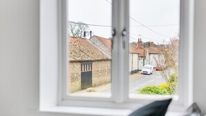 Vista desde una ventana a una calle residencial con casas, un coche blanco y un coche negro estacionados a un lado.