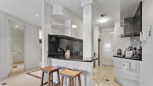 Een moderne keuken met witte kasten, een zwart aanrecht en twee houten stoelen.