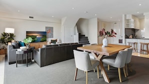 Een moderne woonkamer met een eethoek, een trap en een keuken.