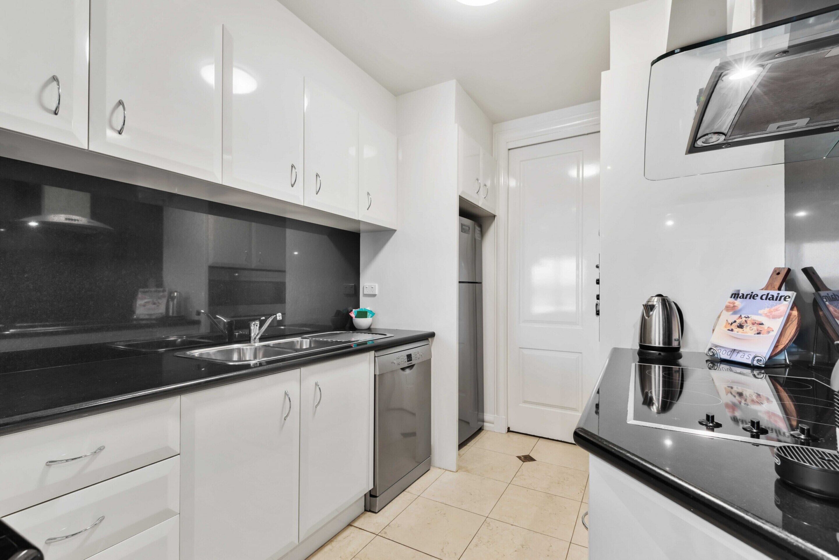 A modern kitchen with white cabinets, a black countertop, stainless steel appliances, and a tiled floor.