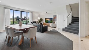 Een moderne woonkamer met een eetgedeelte, een trap en een groot raam met uitzicht op de stad.