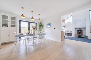 A modern kitchen with a dining area, wooden flooring, and pendant lighting.