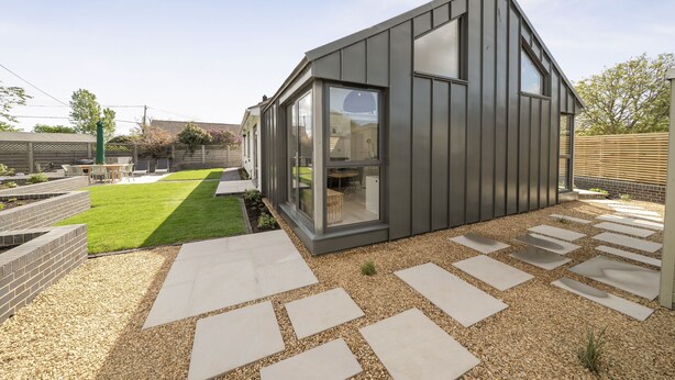 A modern house with a large glass window, a well-maintained lawn, and a stone pathway.