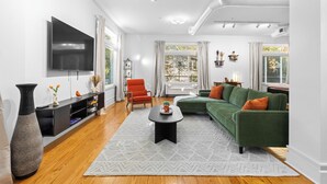 A modern living room with a flat-screen TV, a green sofa, a red armchair, and a large vase. - Cozy Studio Near Plaza+Uptown (Charlotte)
