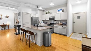 A modern kitchen with white cabinets, a central island, stainless steel appliances, and a bar stool seating area. - Cozy Studio Near Plaza+Uptown (Charlotte)