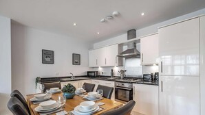 Una cocina moderna con armarios blancos, horno integrado y comedor con mesa de madera para cuatro.