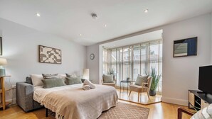 Un dormitorio moderno con una cama grande, una zona de estar con una silla y una mesa, y una televisión.