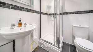 Un baño con cabina de ducha de vidrio, un lavamanos blanco con dispensador de jabón y un inodoro.