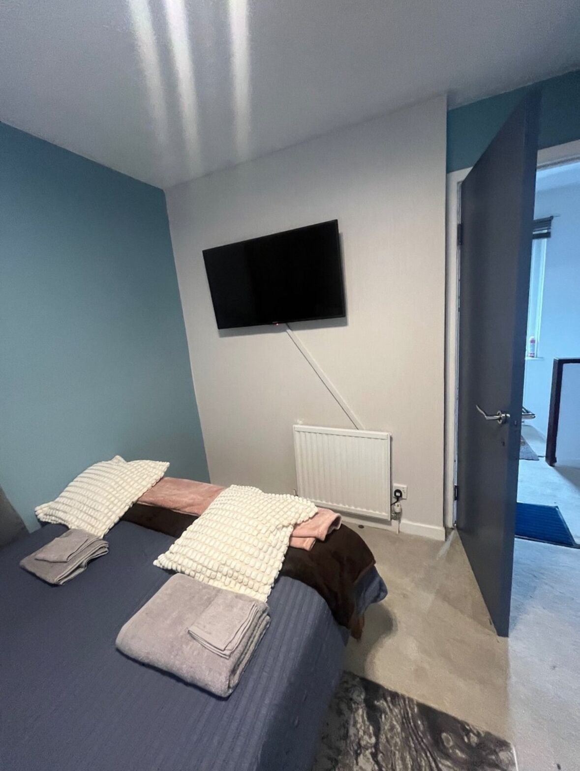 A bedroom with a bed, pillows, a blanket, a TV mounted on the wall, and a radiator.