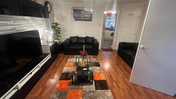 A living room with a TV, black sofa, and a coffee table with flowers.