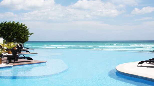 A pool area with lounge chairs and a view of the ocean.