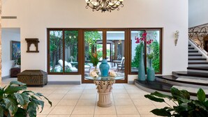A spacious lobby with a glass-top table, a chandelier, and large windows offering a view of the garden.