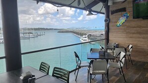 A restaurant with a view of the water and a pier. Tables and chairs are arranged for dining.