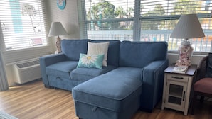 A modern living room with a blue sectional sofa, a small wooden side table, and a window with blinds.