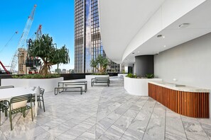 A rooftop terrace with outdoor seating, a reception area, and a view of a tall building and construction cranes in the background. - Brisbane 1BR With Pool, Spa, Sauna and Balcony (Brisbane)