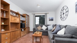 A living room with a grey sofa, wooden cabinets, a wooden coffee table, and a large wall clock. - Home2Book Relaxing Terrace Escape Puerto Lajas (Puerto Lajas)