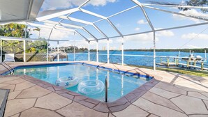An outdoor swimming pool with a clear view of the water and a dock in the background. - Manatee Bay - Waterfront Pool Home & Walk to Bonita Beach (Bonita Springs)