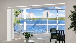 A balcony with a view of a body of water, a chair, a small table, and a plant. - Manatee Bay - Waterfront Pool Home & Walk to Bonita Beach (Bonita Springs)