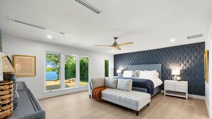 A modern bedroom with a large bed, a sofa, a nightstand, and a view of a garden. - Manatee Bay - Waterfront Pool Home & Walk to Bonita Beach (Bonita Springs)