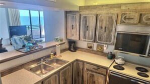 Une cuisine avec des meubles en bois, un évier, une cuisinière et une fenêtre donnant sur l’océan.