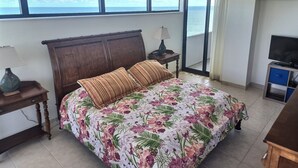 Une chambre à coucher avec un lit, une télévision, une table de chevet et une fenêtre donnant sur la mer.